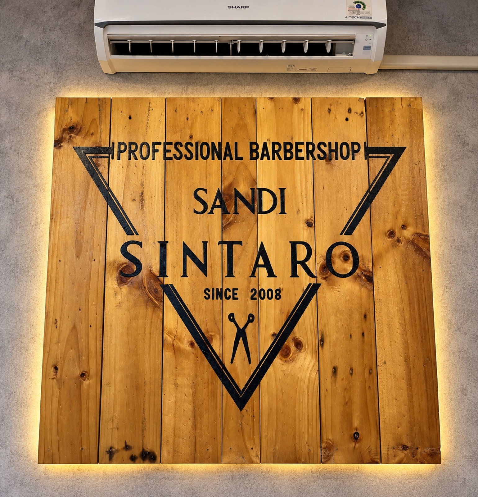 Logo Sandi Sintaro sejak 2008 pada panel kayu dengan pencahayaan hangat